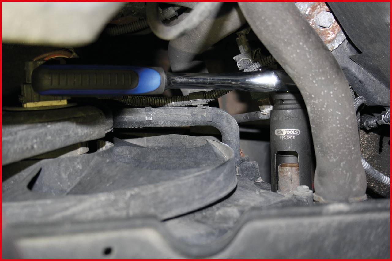 Nahaufnahme eines Werkzeugs, das in einer Werkstatt an einem Fahrzeugmotor arbeitet, Fokus auf Schraubschlüssel und Motorbauteile im Hintergrund.