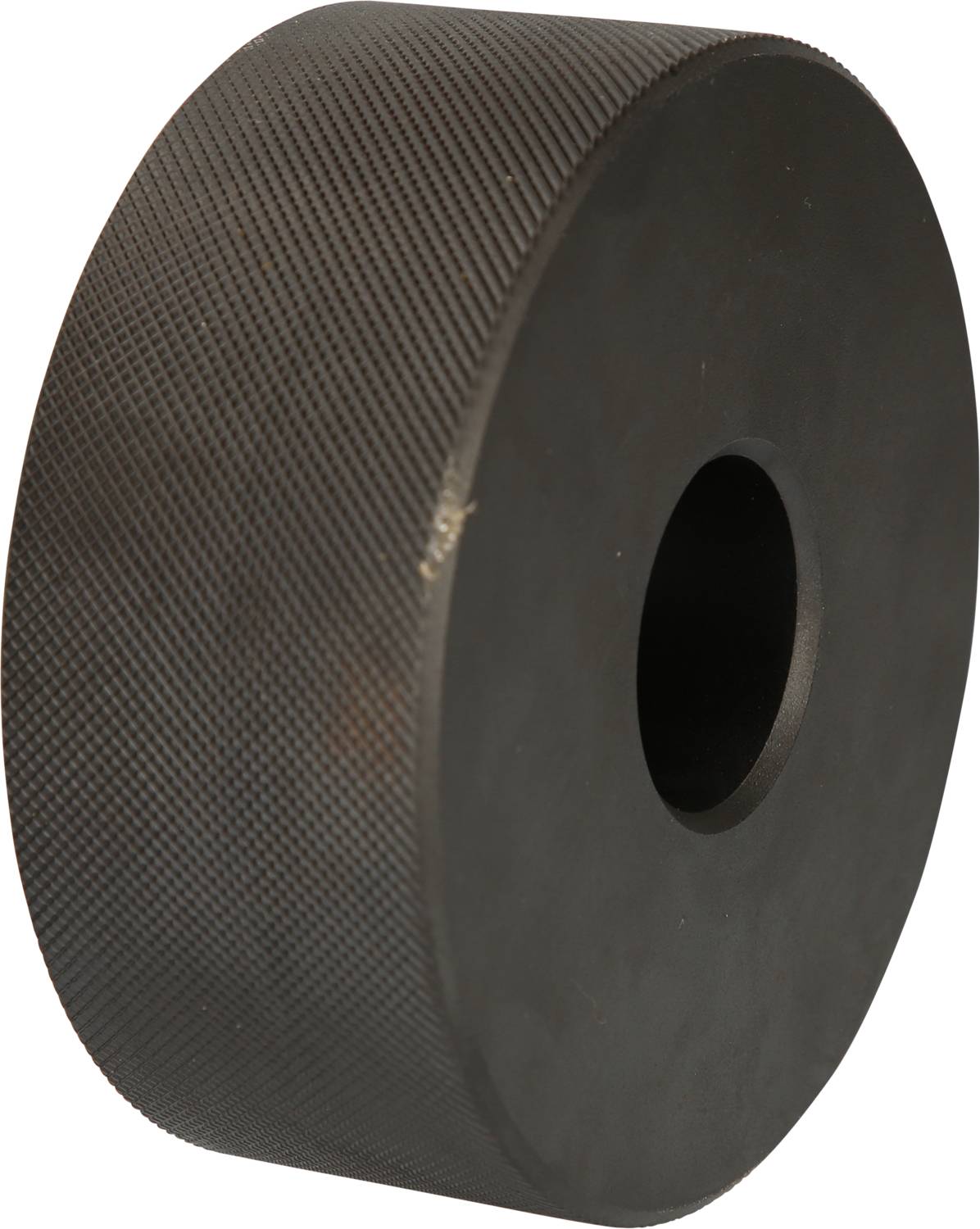 Ein großes, schwarzes, zylindrisches Metallrad mit geriffelter Oberfläche steht vertikal. Es hat ein zentrales Loch.