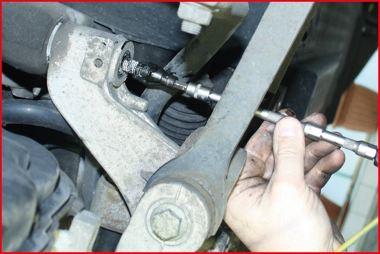 Eine Hand repariert eine Metallkonstruktion mit einer Schraube. Teile eines Motors oder einer Maschine sind sichtbar.