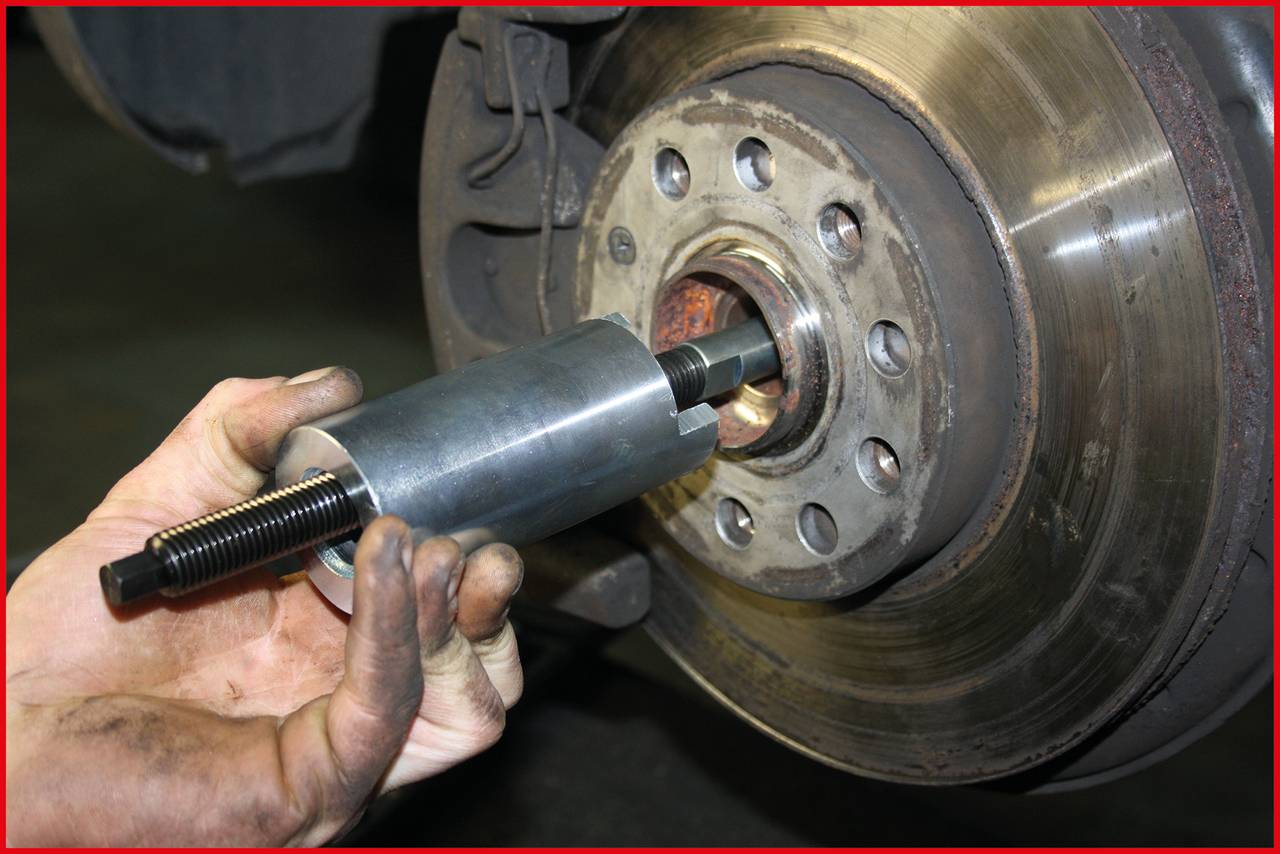 Eine Hand bedient ein Werkzeug zur Montage oder Demontage eines Automobilteils an der Radnabe. Mechanische Arbeit wird gezeigt.