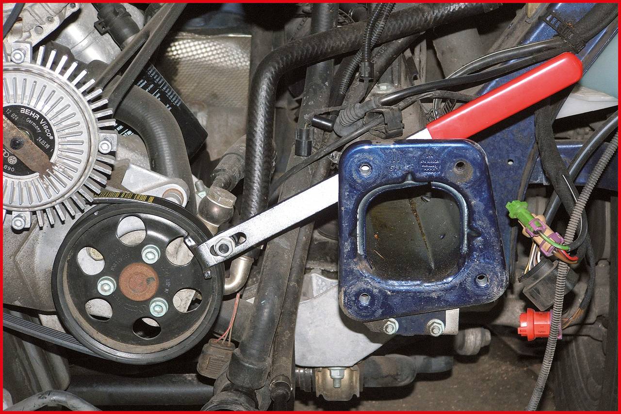 Nahaufnahme eines Motorraums mit Schraubenschlüssel und blauem Halteblech. Links ein Zahnriemenrad und elektrischer Generator.