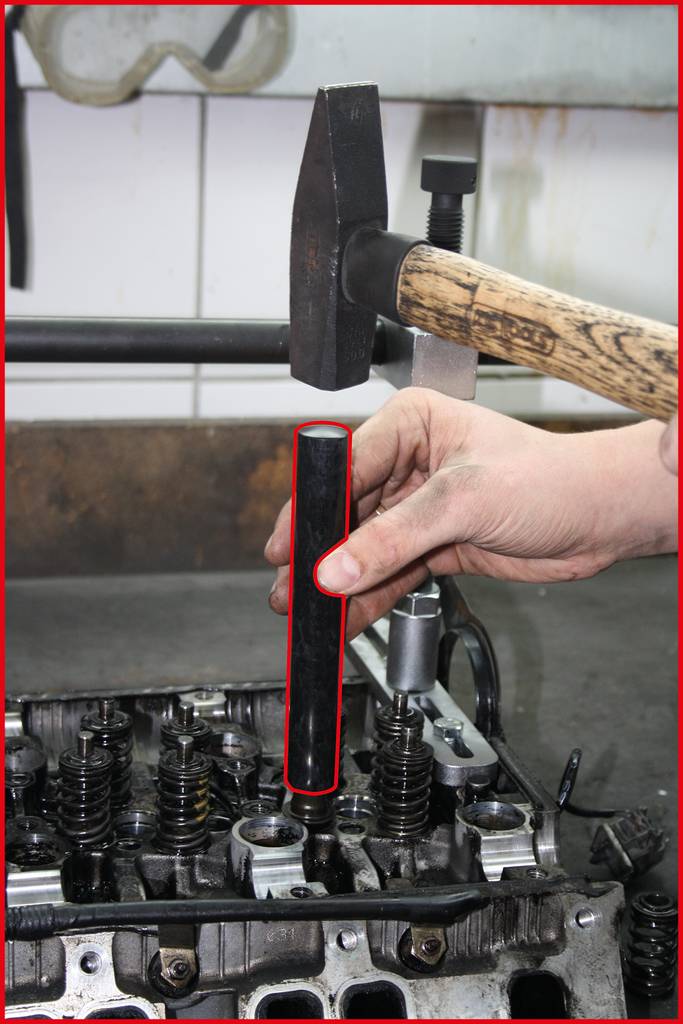 Eine Hand hält ein Ventil, das mit einem Hammer in einen Motorkopf geschlagen wird; zeigt einen Schritt der Motorreparatur.