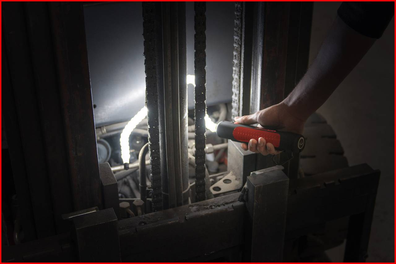 Eine Person leuchtet mit einer Taschenlampe in die Mechanik eines Gabelstaplers, um den inneren Bereich zu inspizieren.