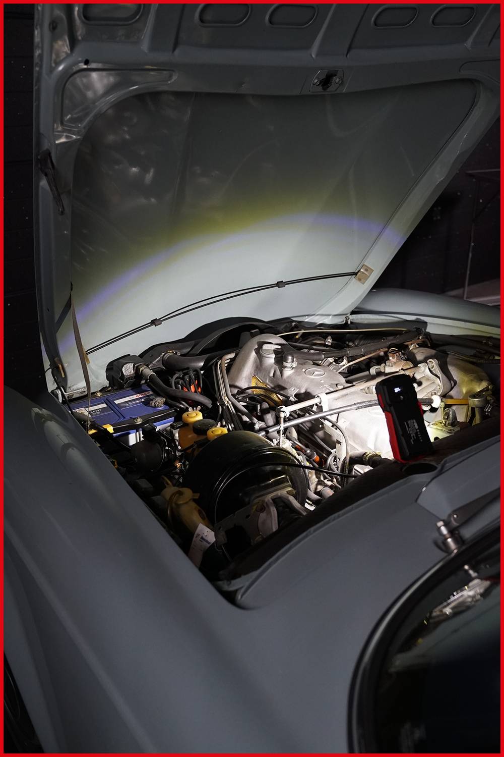 Ein geöffneter Motorraum eines Autos mit sichtbarem Motor und einer Taschenlampe, die das Innere beleuchtet.