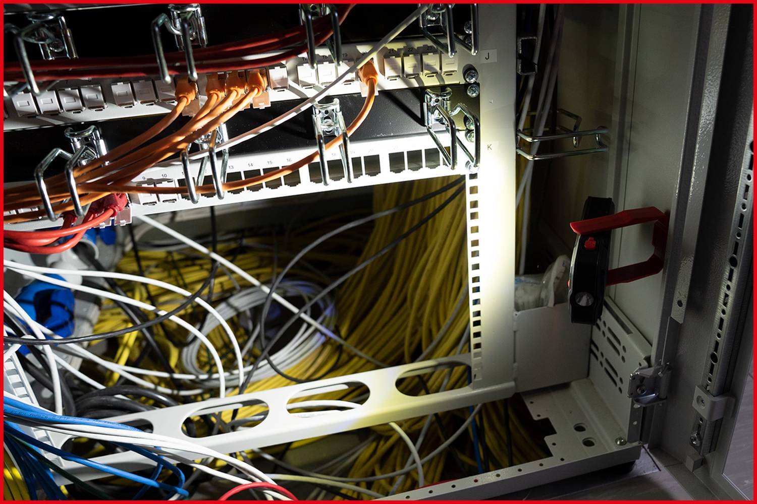 Ein offener Server-Rack zeigt ein Gewirr aus verschiedenen Netzwerkkabeln in verschiedenen Farben, die in Ports eingesteckt sind.