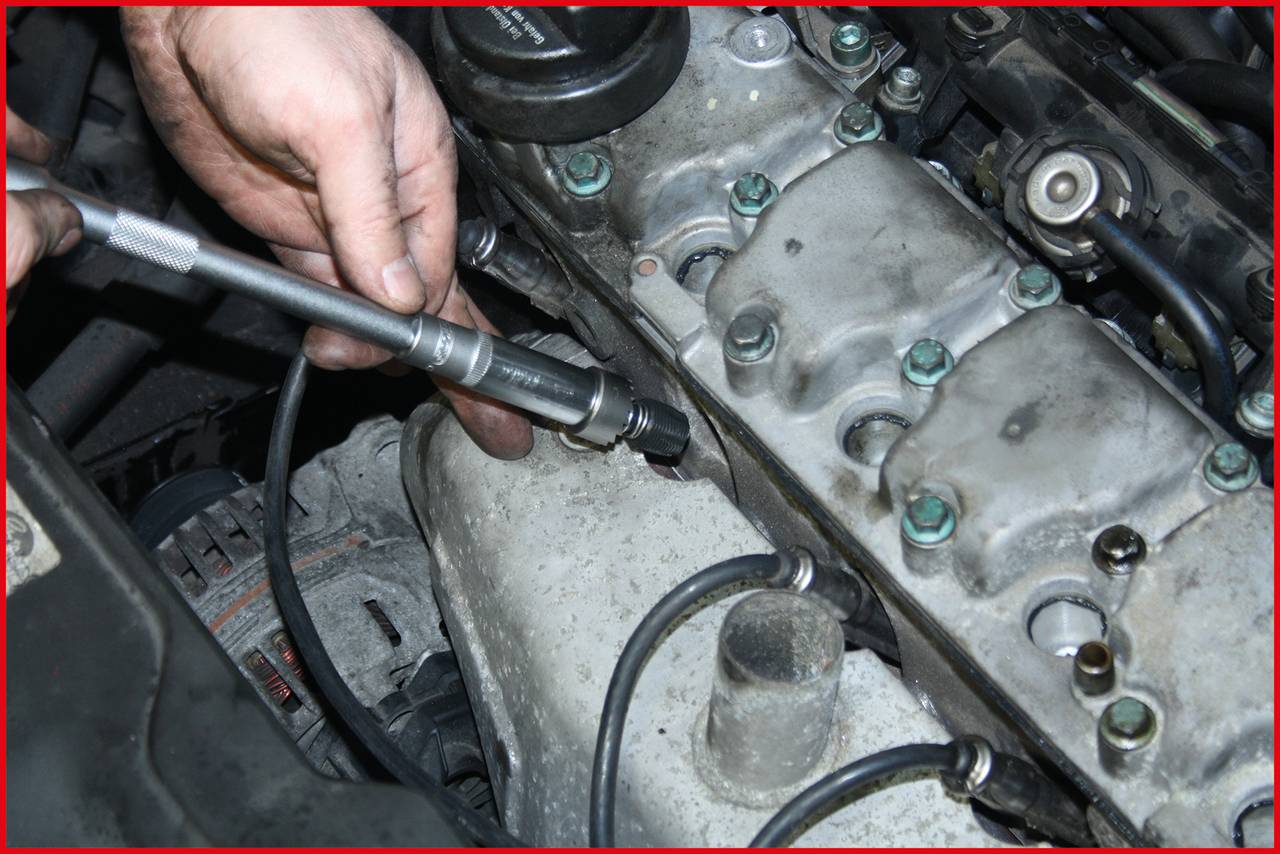 Eine Person verwendet ein Werkzeug, um an einem Automotor zu arbeiten. Das Bild zeigt Details des Motorblocks und umgebende Komponenten.