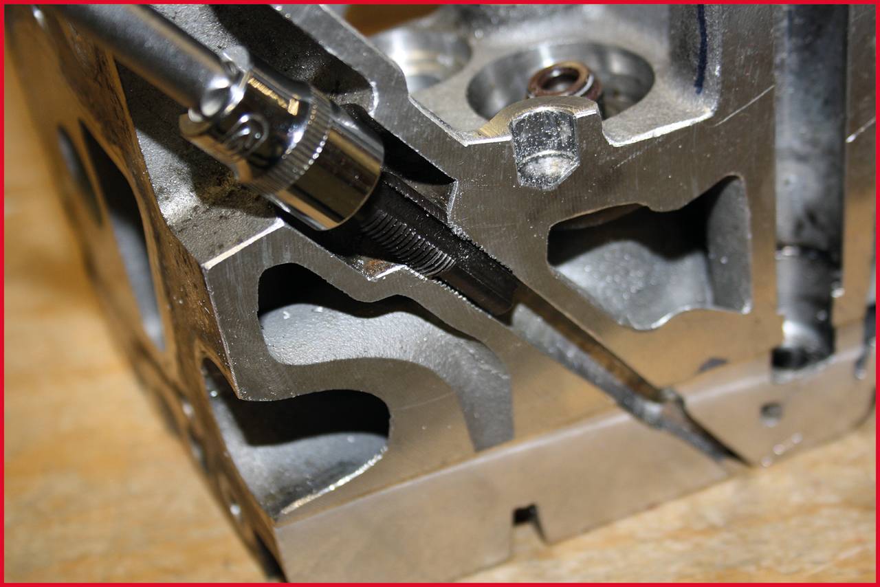 Nahaufnahme eines offenen Motorblocks mit Werkzeug, das einen Bolzen in ein Gewinde einsetzt. Sichtbare mechanische Details und Struktur.