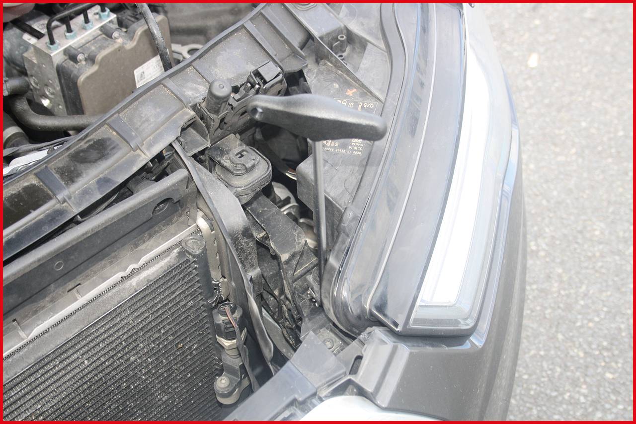 Ein Auto mit geöffneter Motorhaube zeigt den Scheinwerferbereich und Teile des Motors. Der Blinkerhebel ist sichtbar.