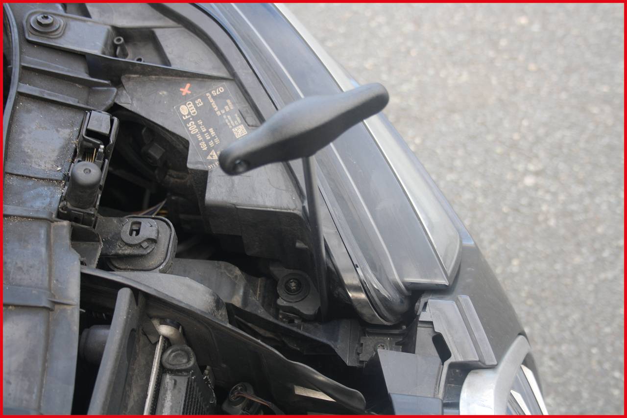 Nahaufnahme eines Autoteils mit freiliegenden Kabeln, sichtbar unter einer aufgehobenen Motorhaube.