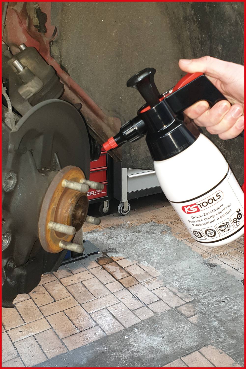 Eine Person hält eine KS Tools Sprühflasche neben einer Autobremsanlage in einer Werkstattumgebung.