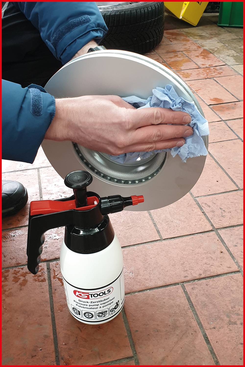 Eine Person reinigt eine Bremsscheibe mit einem Tuch. Davor steht eine Sprühflasche mit einem Reinigungsmittel.