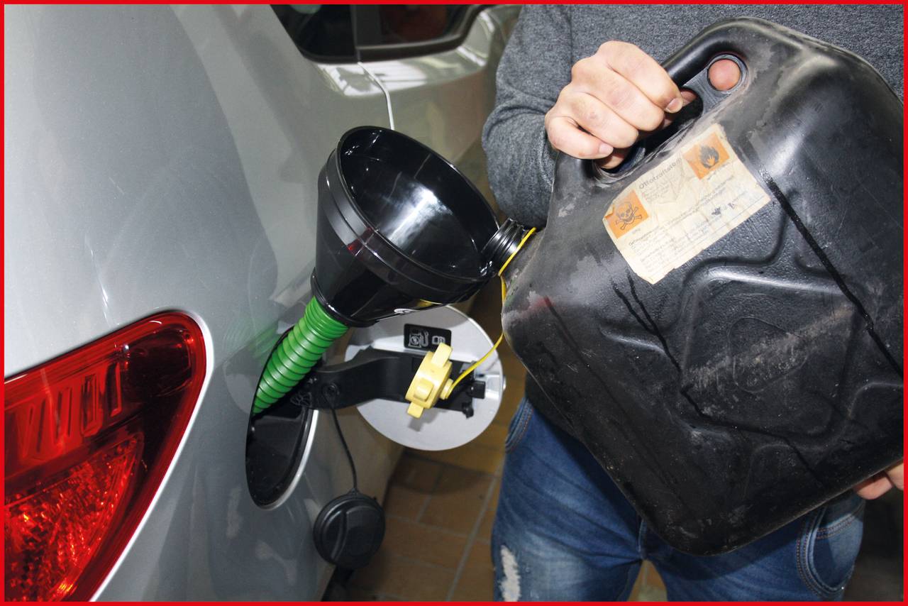 Person füllt Kraftstoff aus einem Kanister in den Tank eines Autos ein. Ein schwarzer Trichter hilft beim Eingießen.