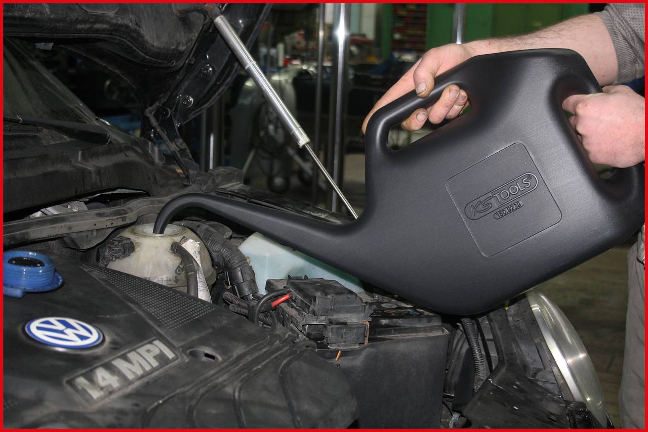 Eine Person füllt Öl in den Motor eines Autos nach. Im Vordergrund ist der Motorraum eines VW mit '1.4 MPI'-Beschriftung zu sehen.