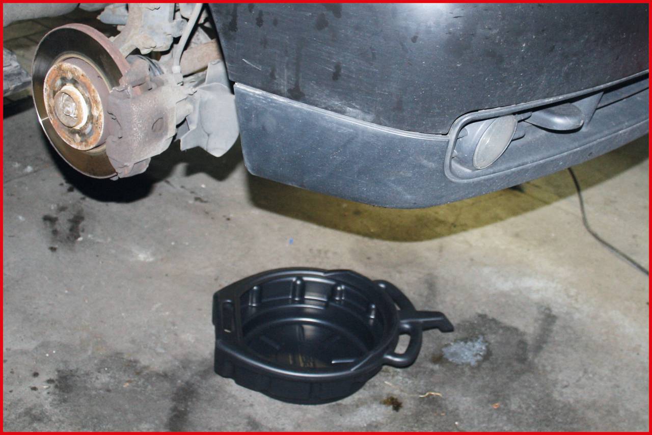 Ein Auto aufgebockt zur Ölablassarbeit. Der Vorderreifen fehlt, und eine schwarze Ölwanne steht darunter für das ablaufende Öl.