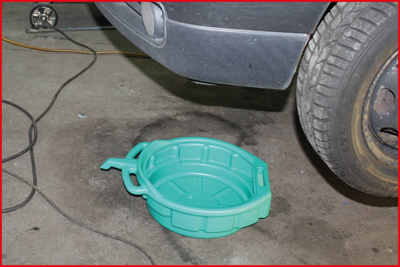 Ein grünes Auffangbecken placed under einem parkenden Auto auf einer Betonfläche. Ein Kabel verläuft entlang des Bodens.