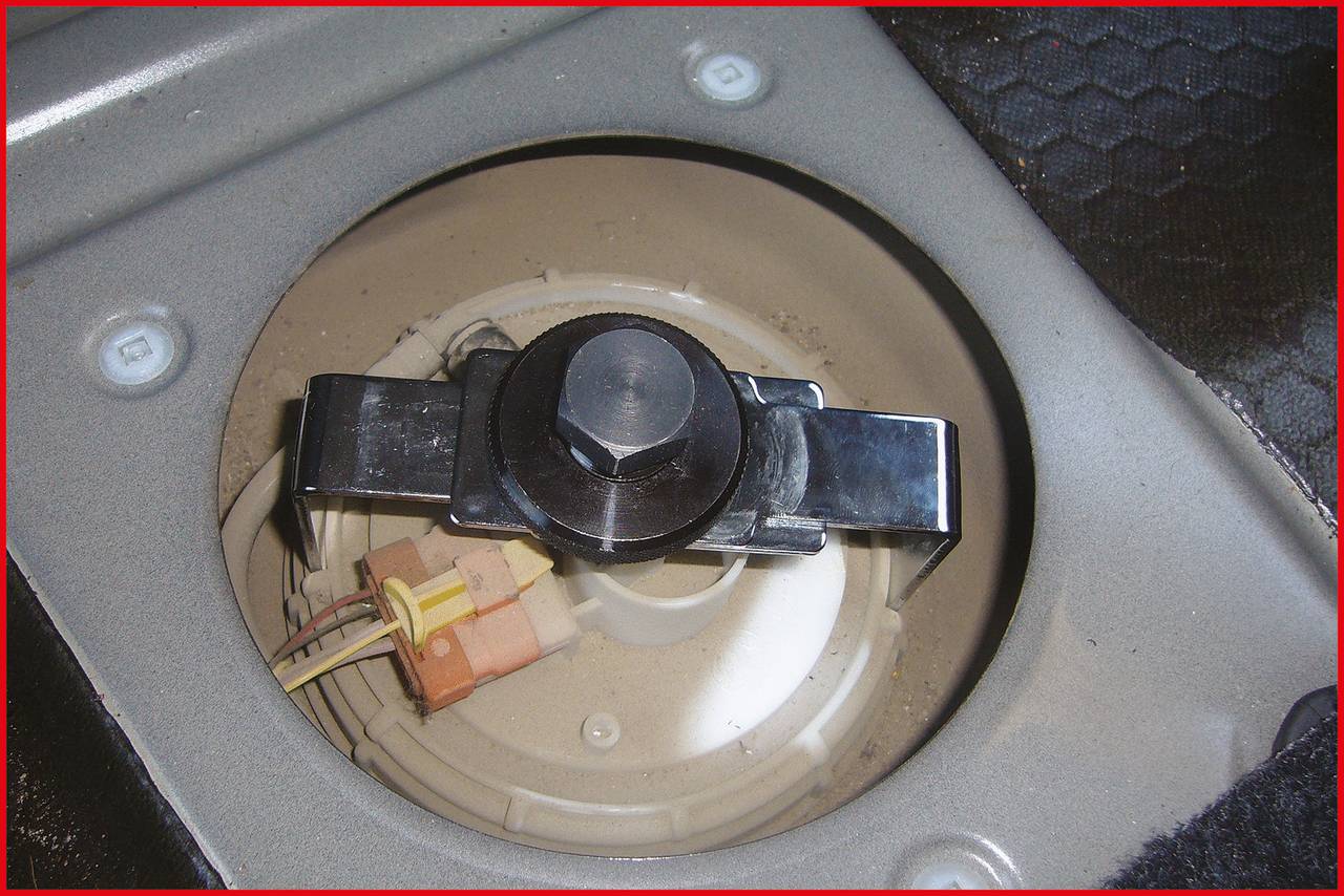 Ansicht eines runden Tankdeckels im Fahrzeug, umgeben von Metallrahmen. Ein Hebel in der Mitte ist befestigt, daneben sichtbare Kabel.