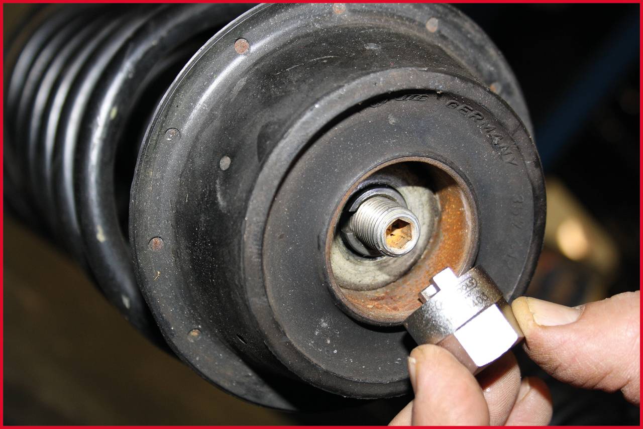 Nahaufnahme eines Autostoßdämpfers mit einer Hand, die eine Mutter hält, um sie zu befestigen. Fokus auf Mechanik und Funktion.