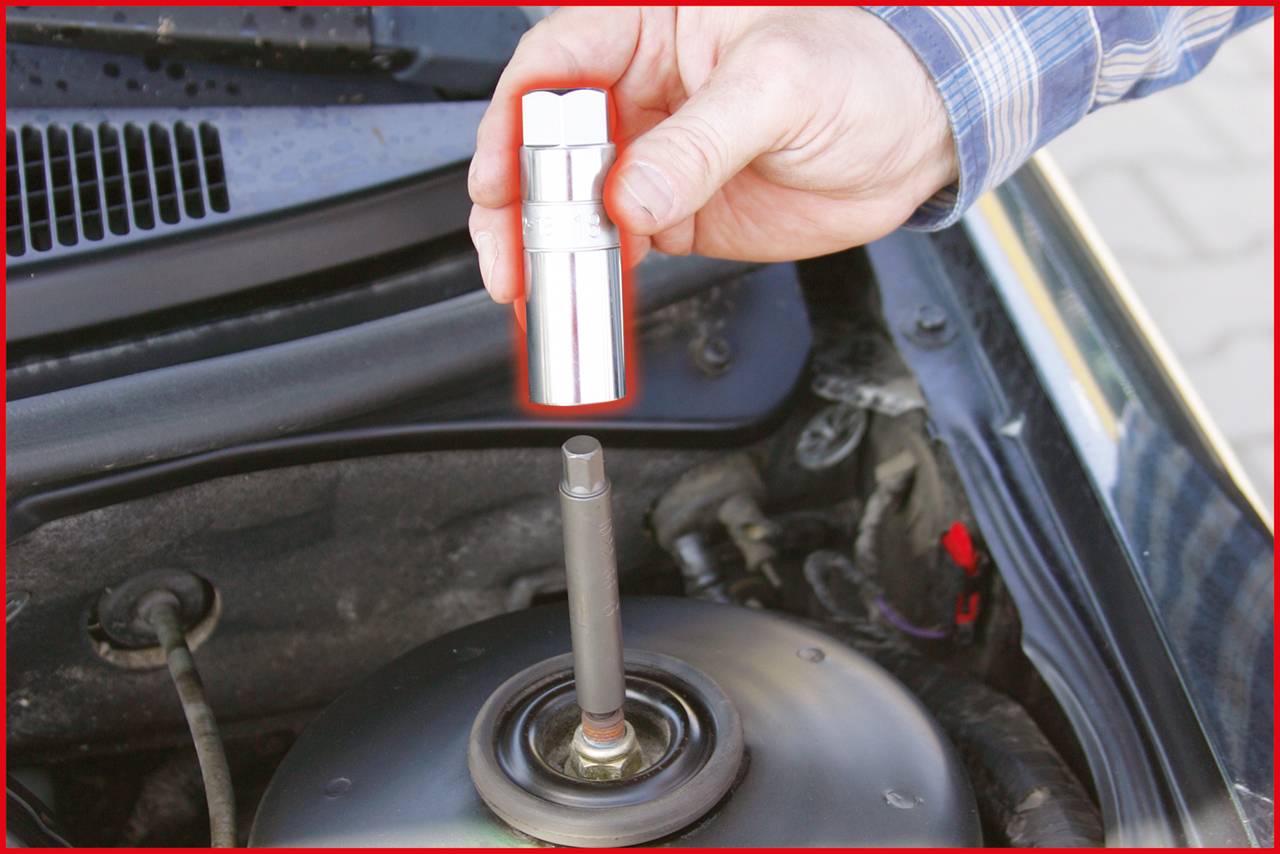 Person hält eine metallische Stecknuss über einer Stoßdämpferverschraubung in einem Auto. Fokus auf Werkzeugeinsatz im Motorraum.