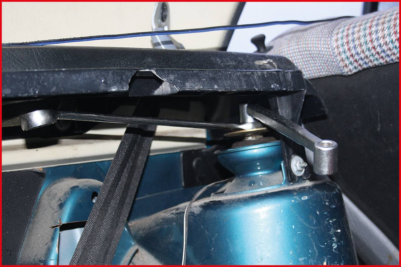 Nahaufnahme eines Autositzes, Fokus auf den Mechanismus zur Neigungseinstellung der Rückenlehne. Ein Metallhebel ist sichtbar.