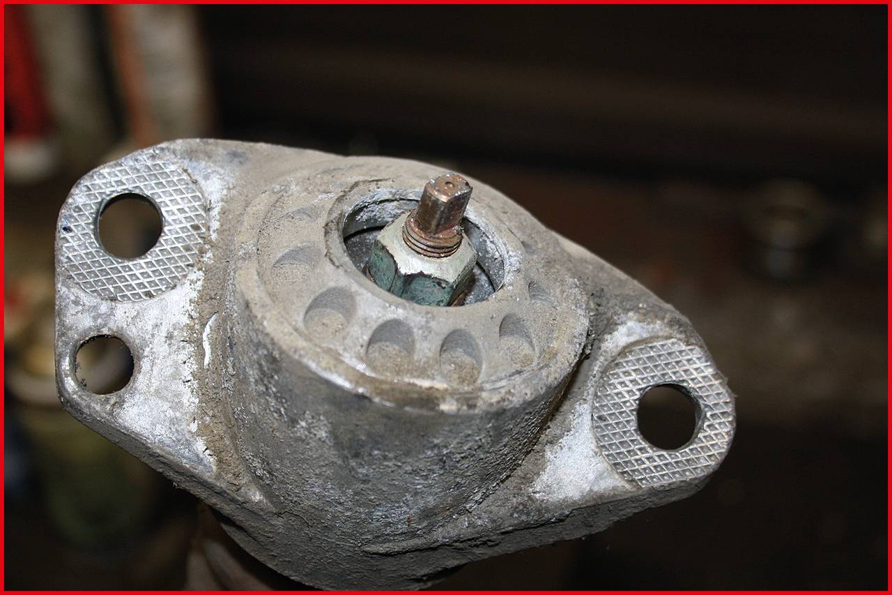 Nahaufnahme eines rostigen Metalllagers mit Verankerungslöchern, wahrscheinlich Teil einer Maschine oder eines Fahrzeugs.