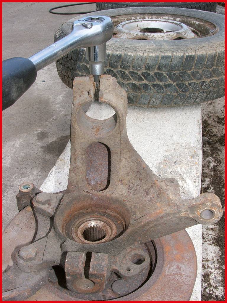 Eine Ratsche wird an einem alten, rostigen Autoteil verwendet. Im Hintergrund liegt ein gebrauchter Reifen auf dem Boden.