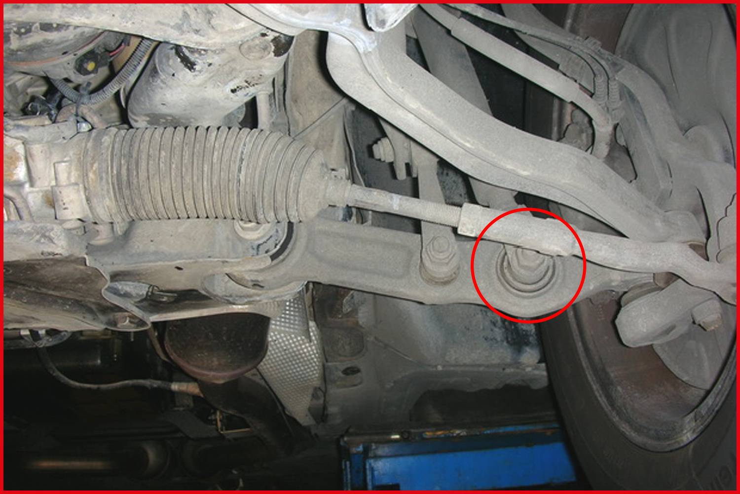 Untere Ansicht eines Autos zeigt das Fahrwerk mit Fokus auf die beschädigte oder lose Verbindung der Spurstange, rot eingekreist.