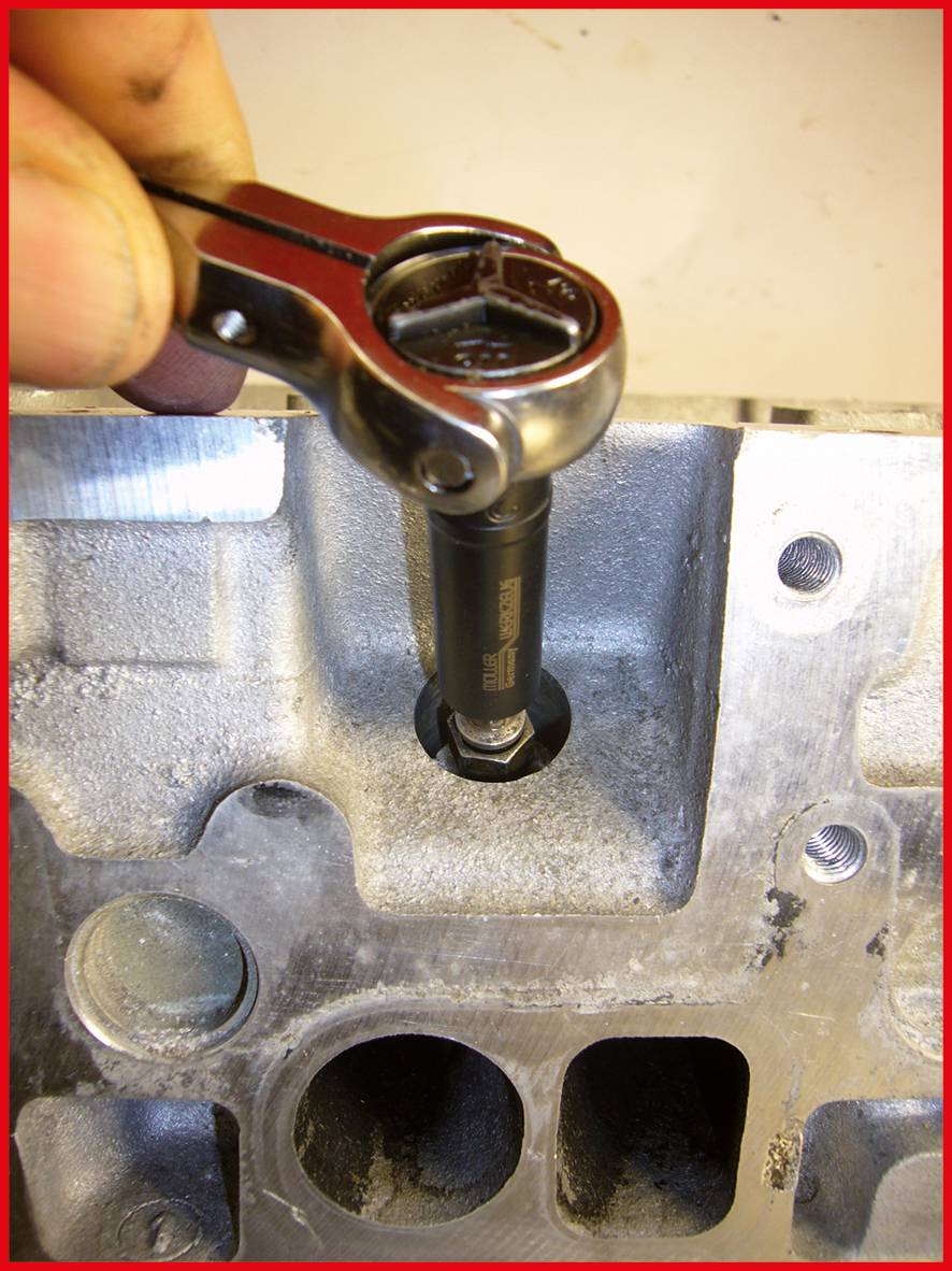 Eine Hand hält einen Steckschlüssel, der eine Schraube an einem Motorblock anzieht oder löst.