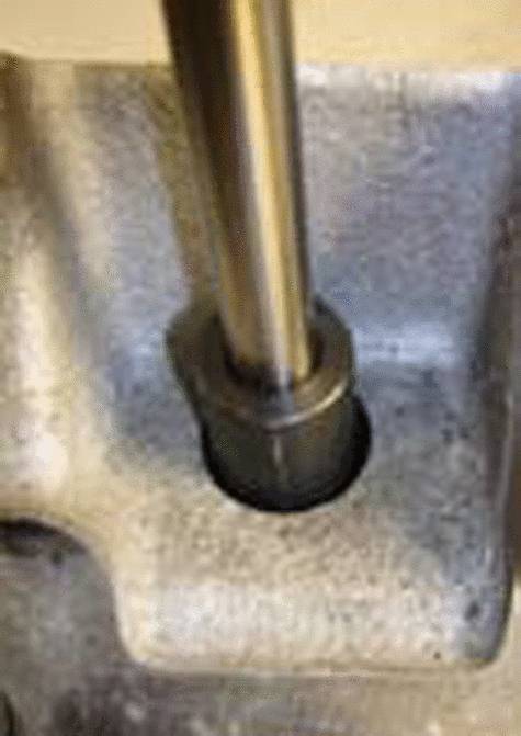 Metallisches Bauteil mit vertikalem zylindrischem Stab in einer robusten, rechteckigen Halterung montiert.
