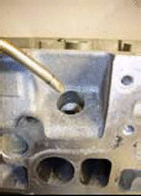 Ein metallisches Werkzeug zeigt auf eine Öffnung in einem maschinellen Bauteil, das aus grauem Metall besteht.