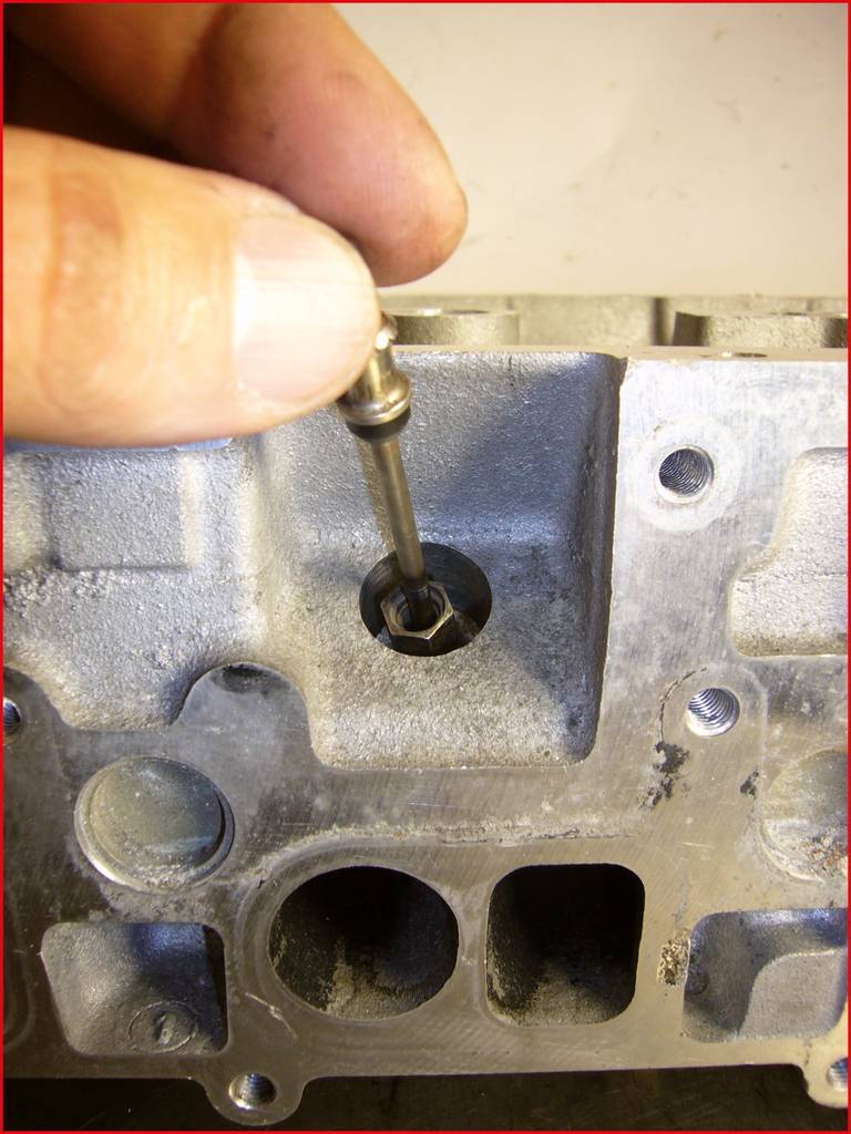 Nahaufnahme einer Hand, die eine kleine Metallstange hält und über einem Motorteil positioniert. Der Fokus liegt auf der Mechanik.