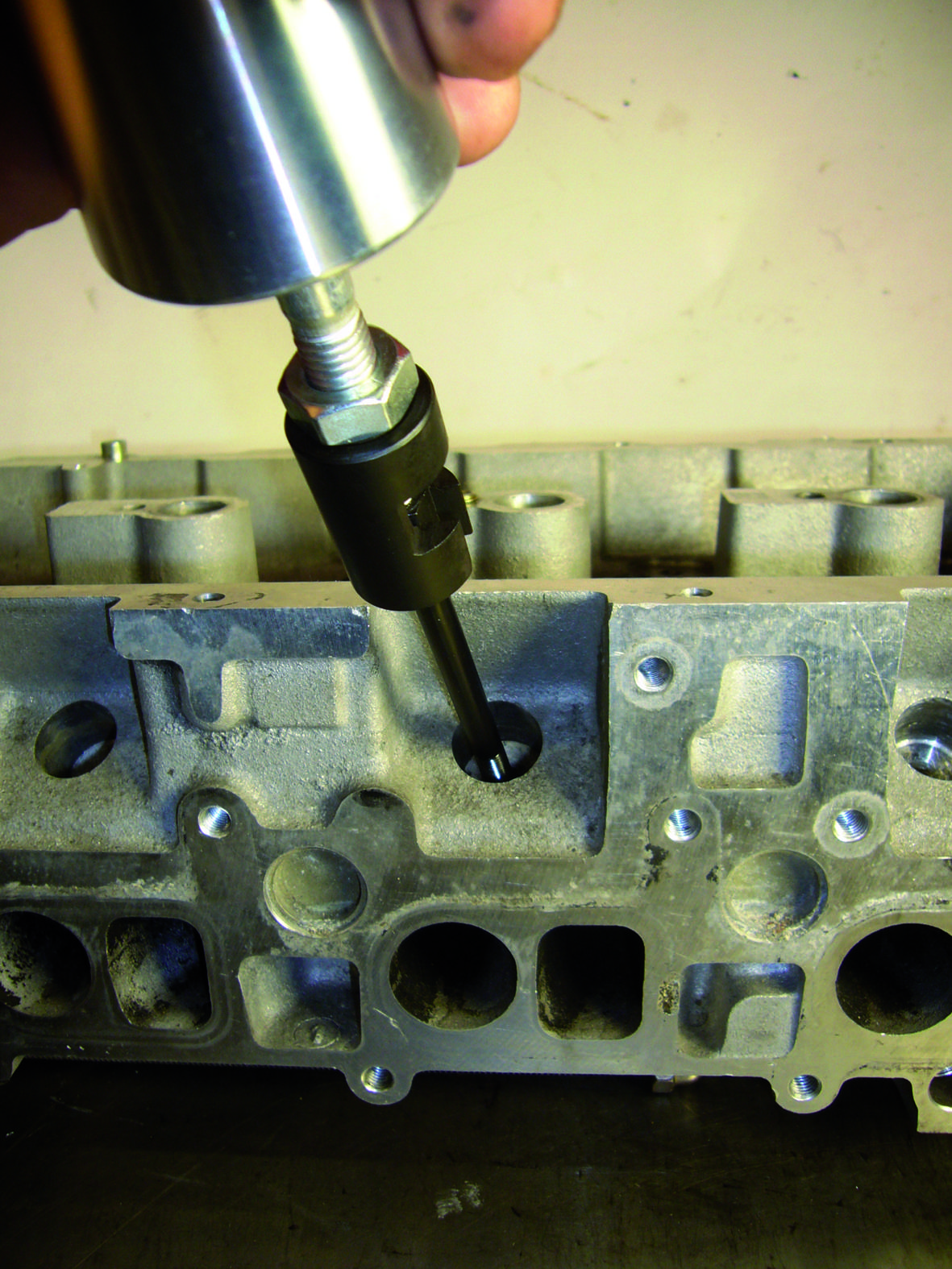 Eine Metallvorrichtung wird in einen Zylinderkopf eingebaut. Im Hintergrund sind Details des Zylinderkopfs sichtbar.