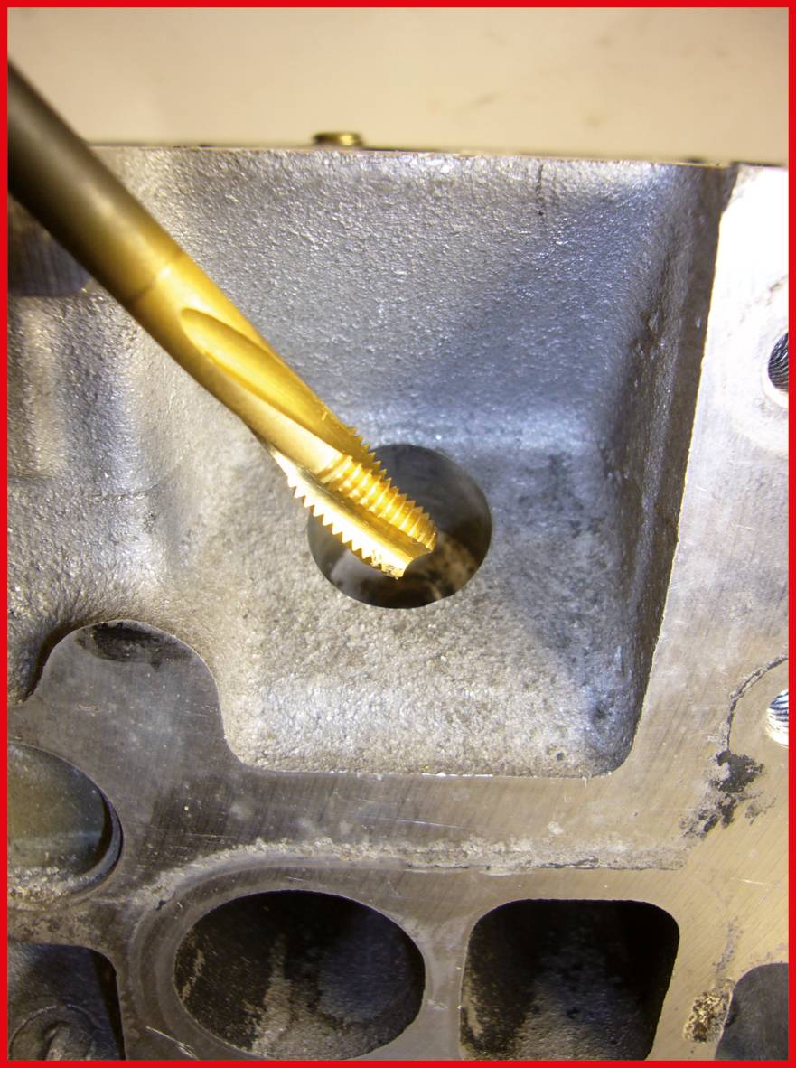 Ein goldfarbener Gewindebohrer bearbeitet ein Loch in einem Metallmotorblock, um ein neues Gewinde zu schneiden.