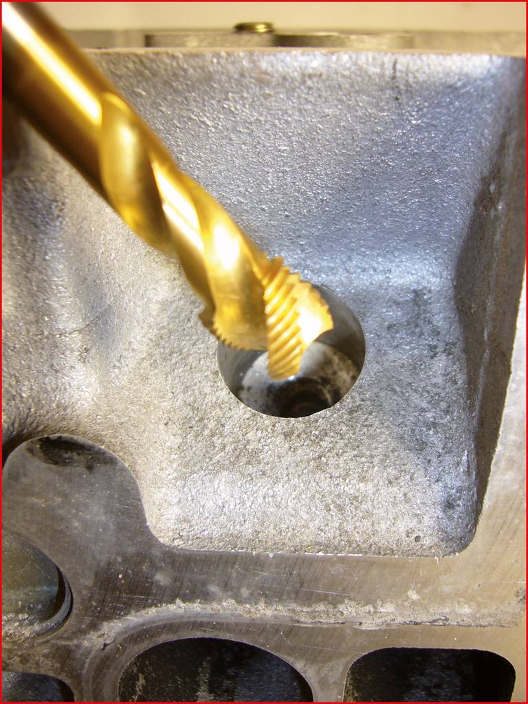 Ein goldener Bohrer bearbeitet ein Gewinde in einem metallischen Block.