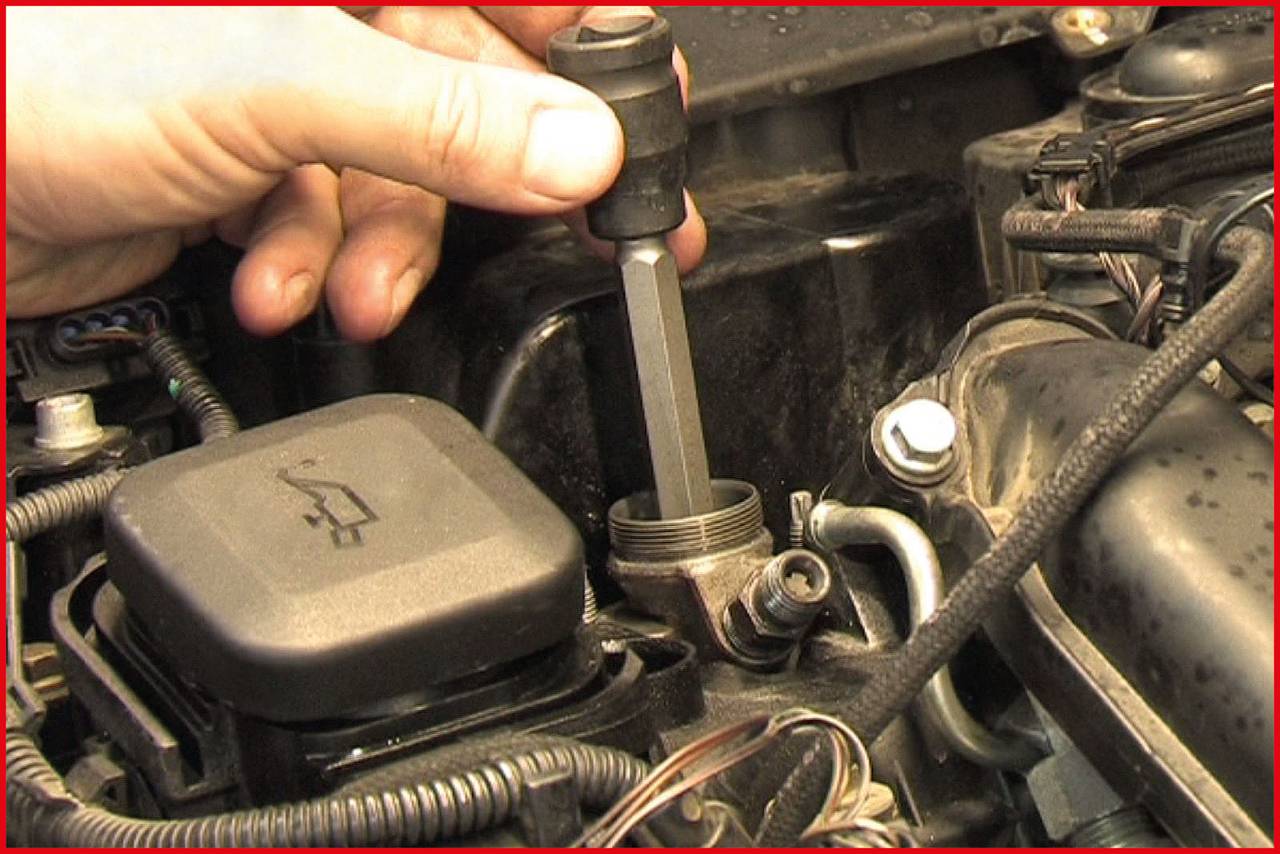 Eine Hand benutzt ein Werkzeug, um einen Teil im Motorraum eines Autos zu überprüfen.