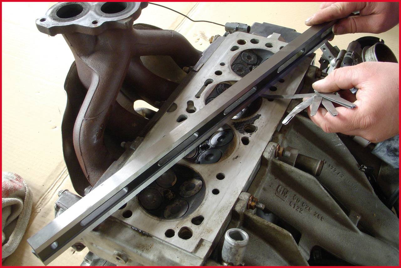 Person überprüft Zylinderkopf eines Motors mit Messwerkzeug, der Motorblock ist unvollständig montiert.
