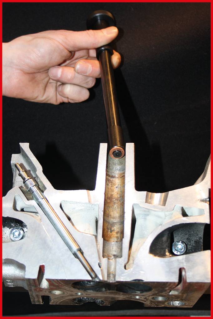 Eine Hand hält eine Metallstange über einem ausgearbeiteten Metallteil, das möglicherweise Teil eines Motors ist.