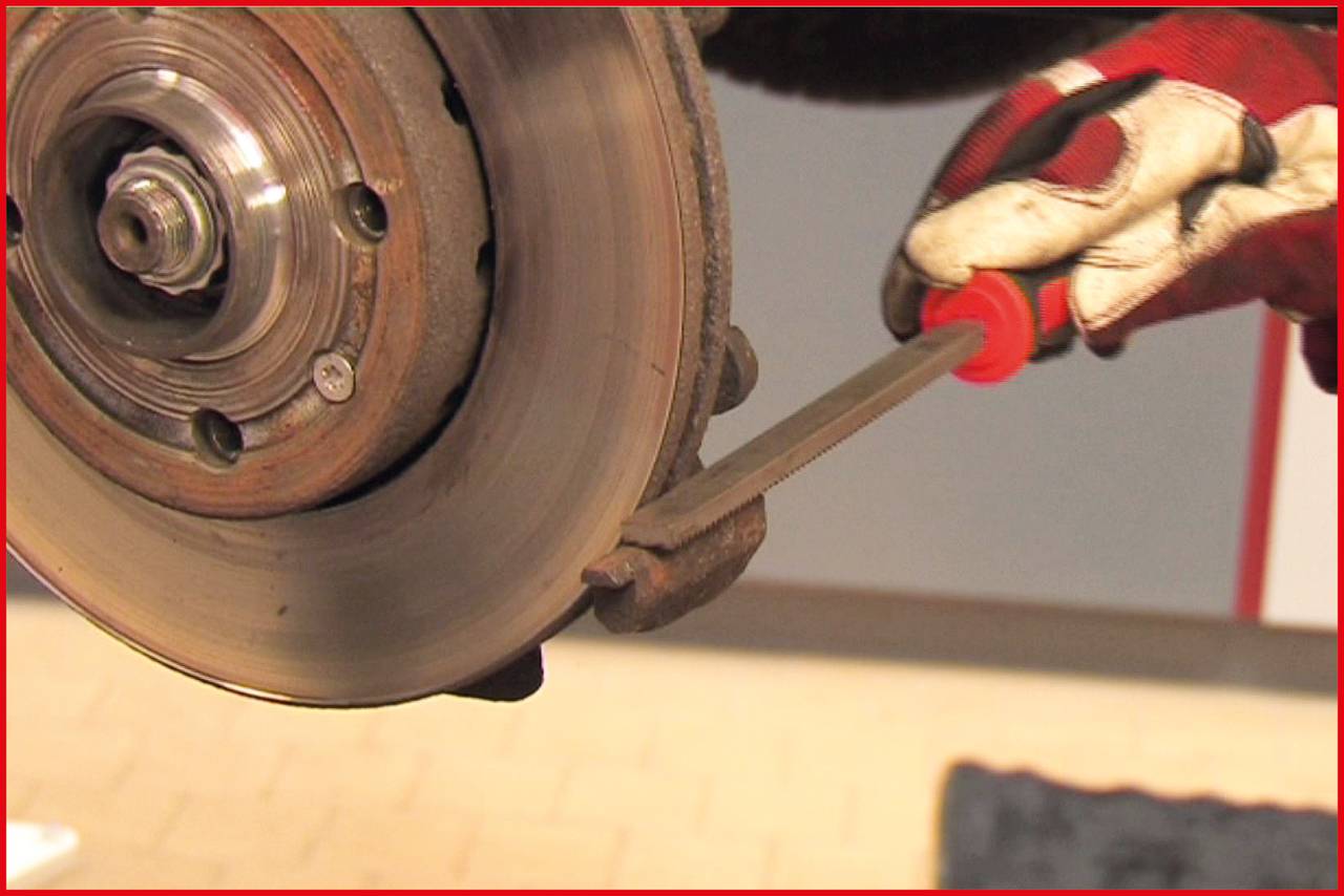 Ein Mechaniker überprüft mit einem Schraubendreher den Zustand einer Bremsscheibe an einem Fahrzeug.