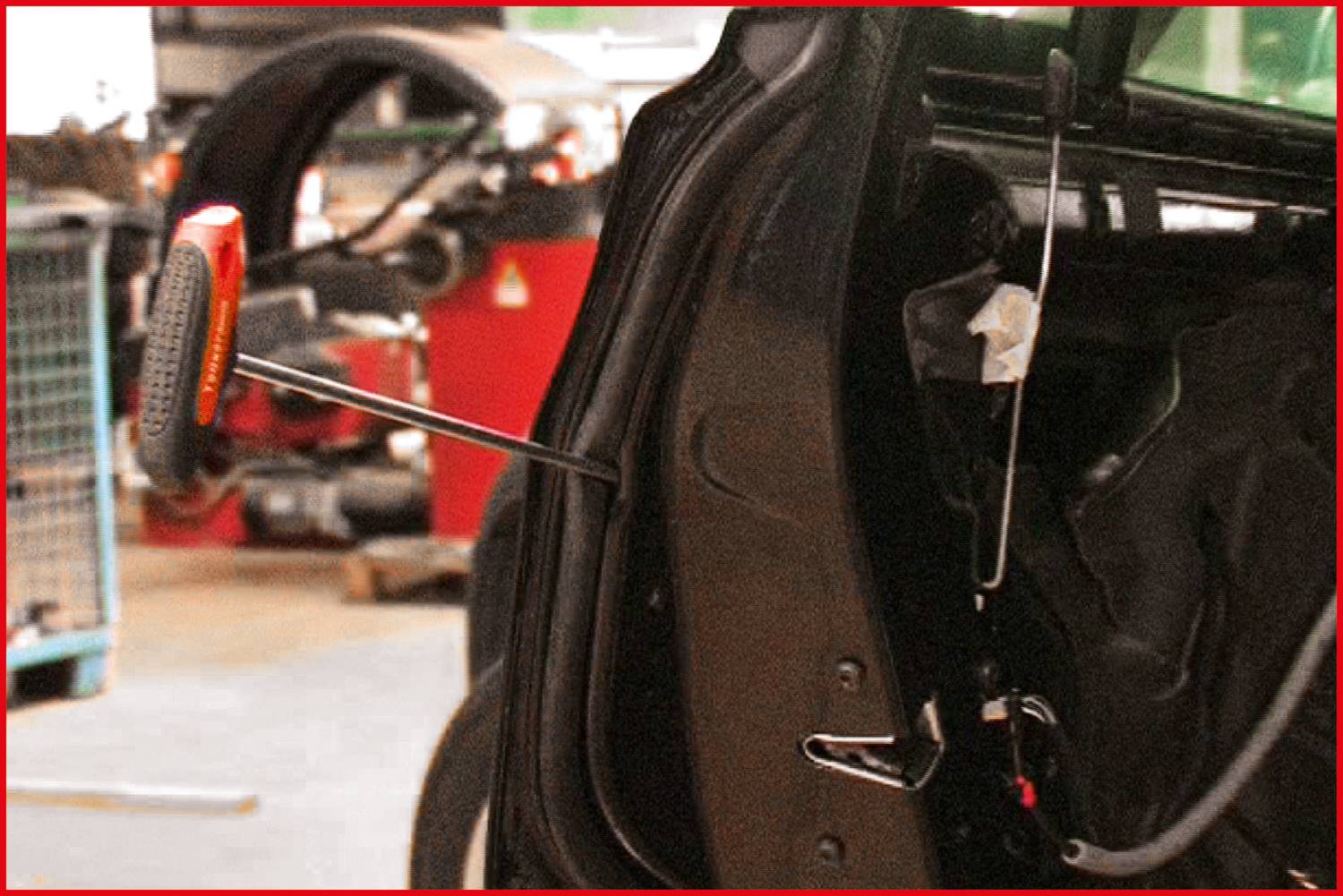 Ein schwarzes Auto mit geöffneter Tür in einer Werkstatt. Ein oranger Werkzeuggriff ragt aus der Türverkleidung, deutet auf Reparaturen hin.