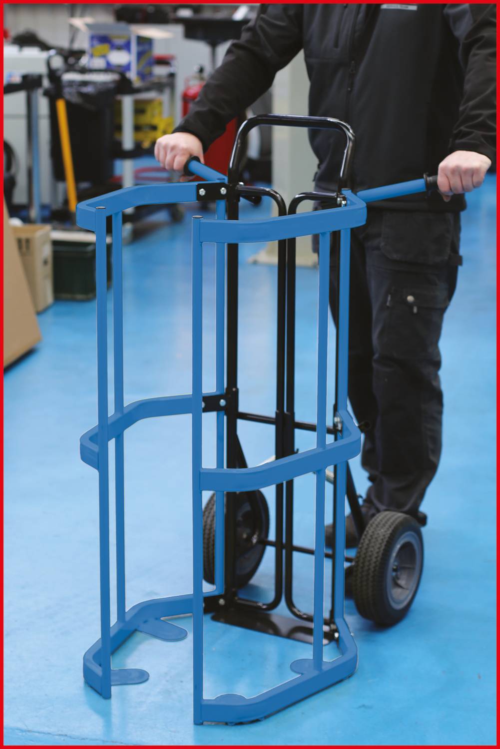 Eine Person schiebt einen blauen Transportwagen auf einem blauen Werkstattboden. Im Hintergrund sind Werkstattutensilien sichtbar.