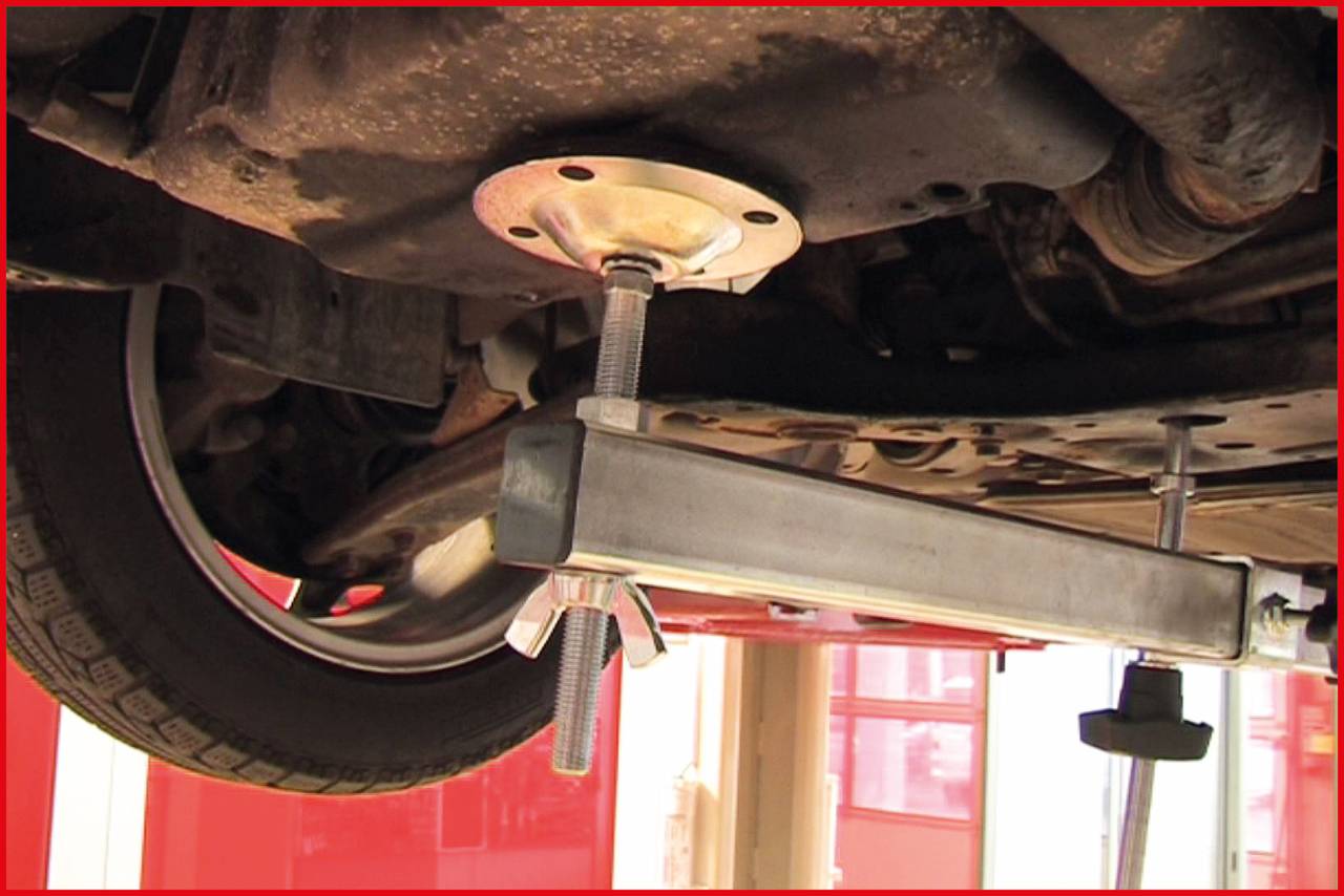 Ein Autoreifen wird von einer hydraulischen Hebevorrichtung in einer Werkstatt angehoben. Der Fokus liegt auf der Hebeanlage unter dem Fahrzeug.