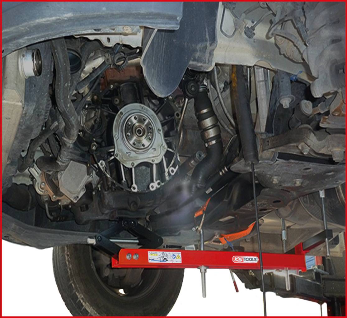 Ein Auto von unten betrachtet, zeigt das freiliegende Getriebe und verschiedene mechanische Komponenten während einer Reparaturphase.