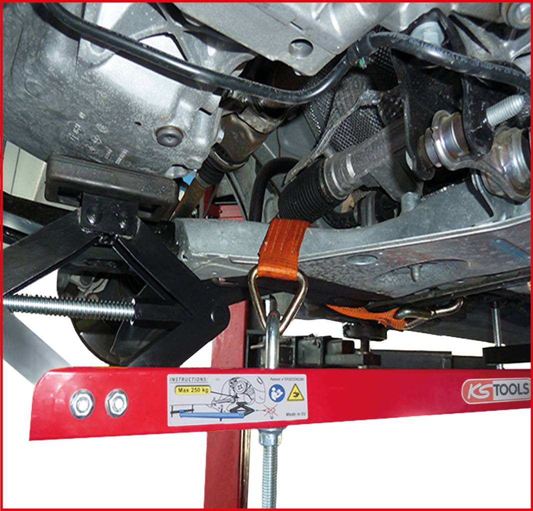 Unterseite eines Autos, das auf einem Hebebühne-Rahmen gesichert ist. Ein orangener Gurt fixiert Teile des Motors an der Konstruktion.