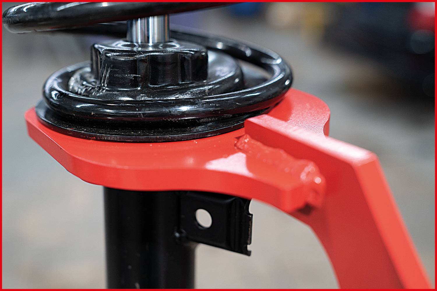 Nahaufnahme eines Autostoßdämpfers mit einer roten Halterung. Der Stoßdämpfer ist teilweise montiert. Mechanische Umgebung im Hintergrund.
