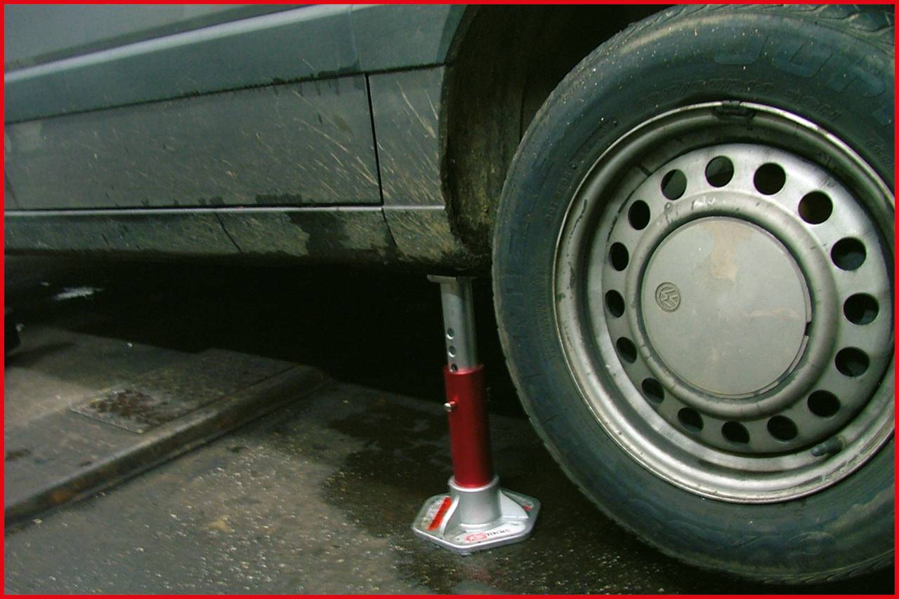 Ein Auto steht leicht angehoben auf einem Wagenheber. Der Boden ist nass und das Auto ist schmutzig.