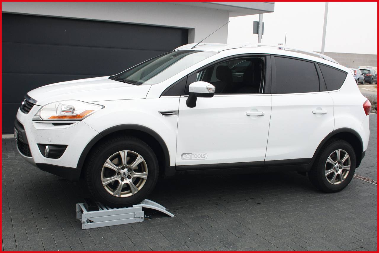 Ein weißes SUV-Park auf einer Einfahrt vor einer Garage. Das rechte Vorderrad steht auf einer Rampe.