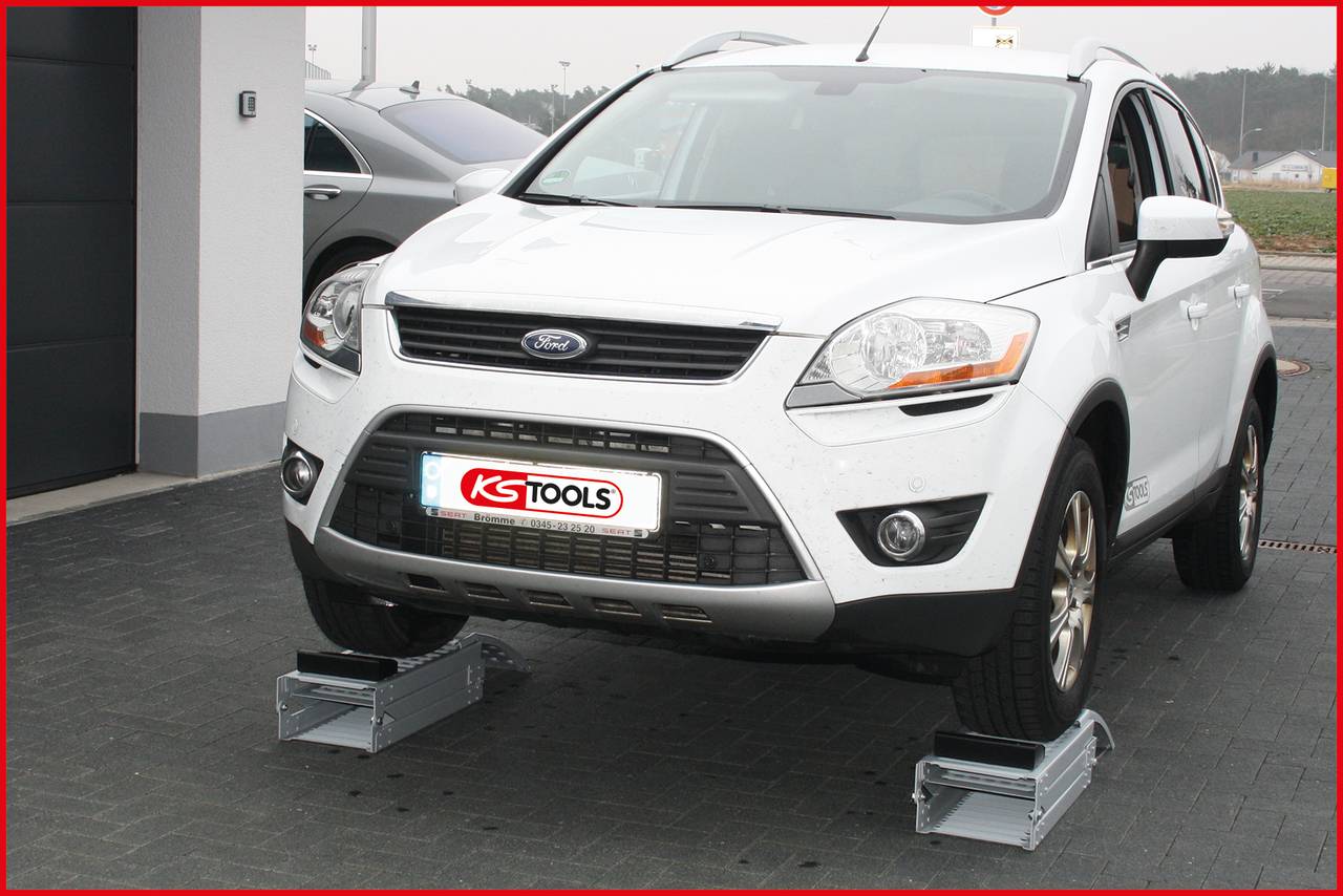 Ein weißes Auto steht auf zwei Ramps von KS Tools, angehoben für Reparaturarbeiten. Im Hintergrund ist ein weiteres Fahrzeug sichtbar.