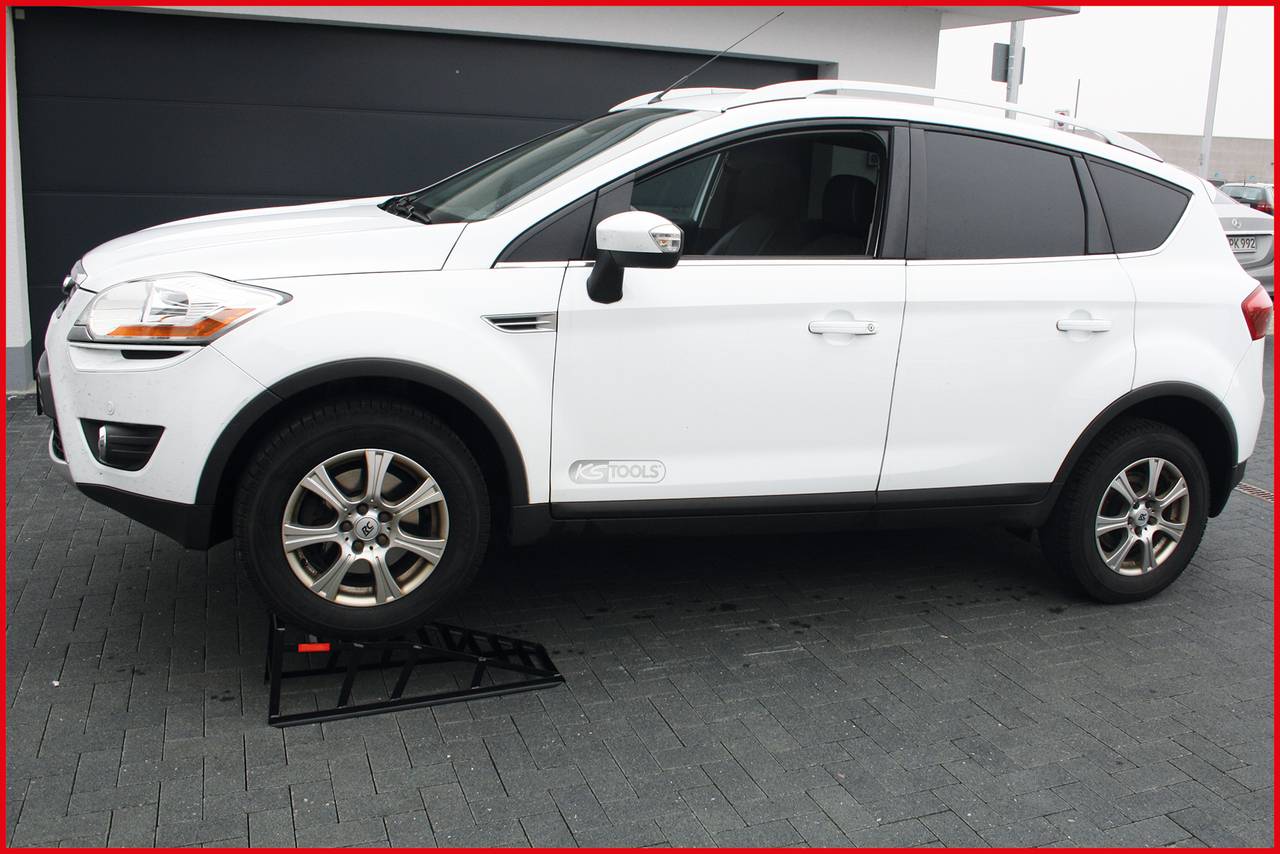 Ein weißes SUV-Fahrzeug steht schräg an einer Rampe auf einer asphaltierten Fläche vor einer Garage.