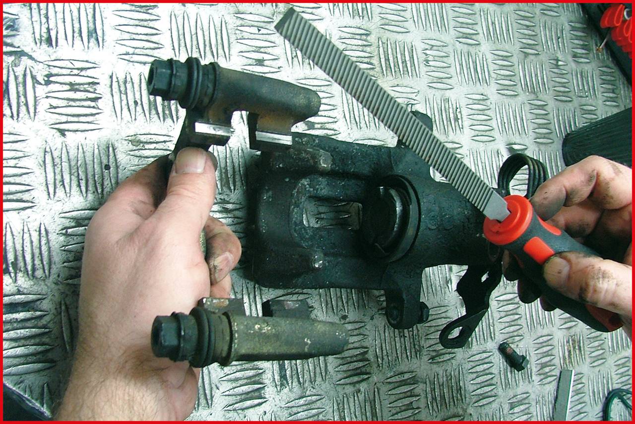 Zwei Hände arbeiten an einer Fahrzeugbremse. Eine Hand hält eine Metallfeile, die andere hält ein Bremsbauteil auf einem Metallboden.