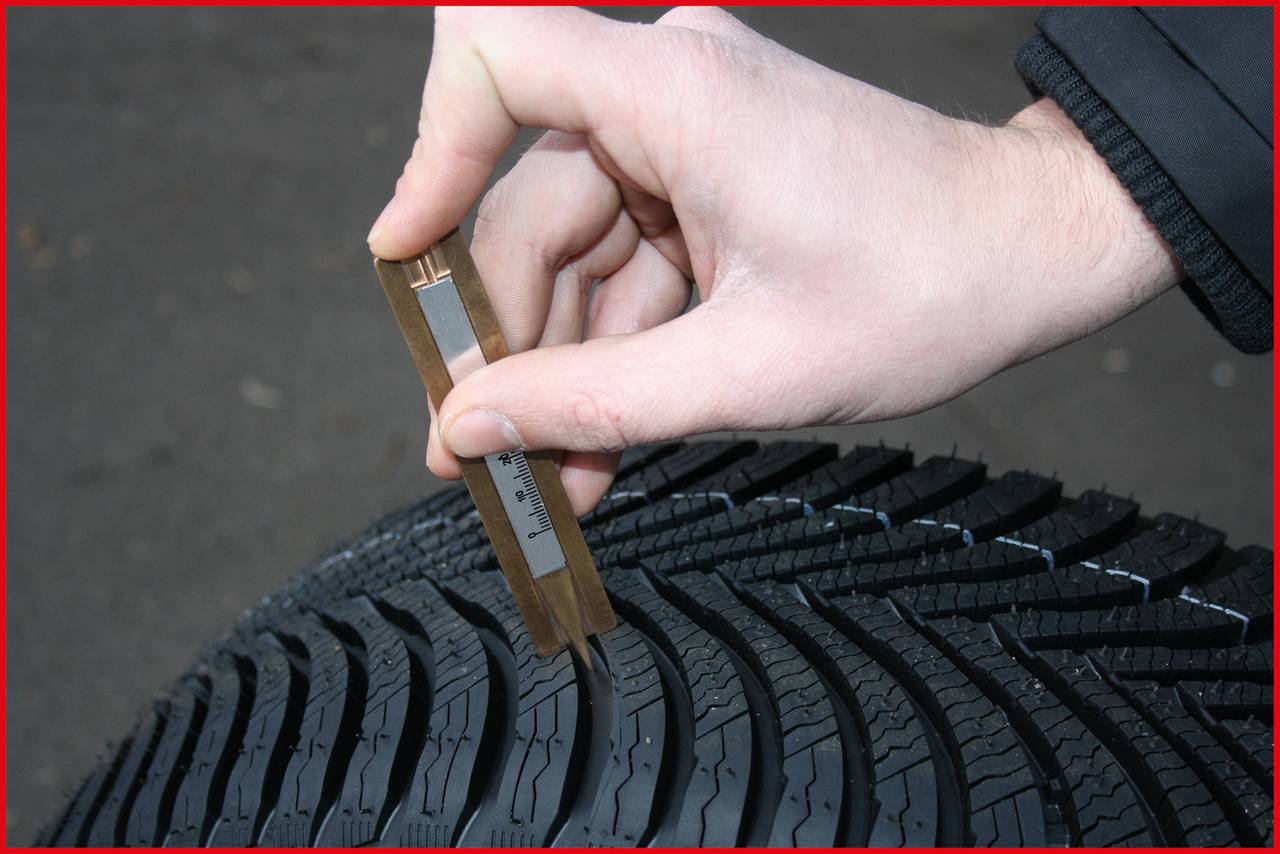 Eine Hand überprüft mit einem Messgerät die Profiltiefe eines Autoreifens auf die Mindestanforderungen für Sicherheit im Straßenverkehr.
