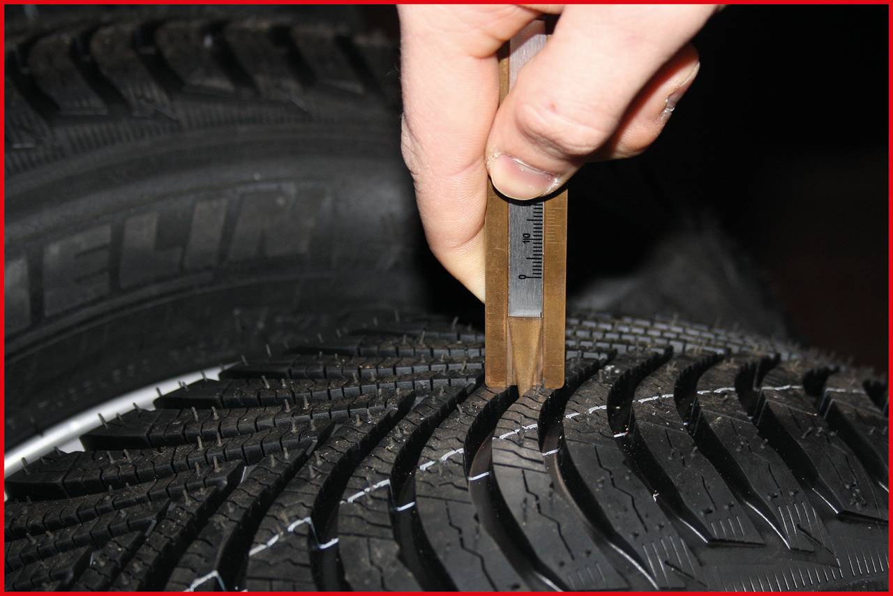 Eine Hand misst die Profiltiefe eines Autoreifens mit einem Messgerät.